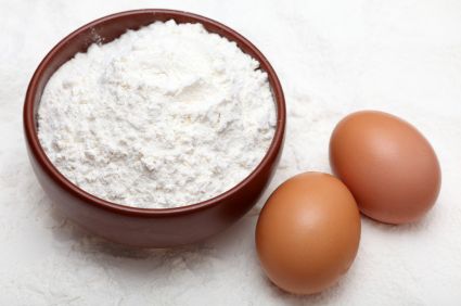 A bowl of white flour with two whole eggs placed on a surface dusted to flour.