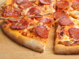 Slices of pepperoni pizza, central to the Port Chester pizza debate, on a wooden surface with a focus on the melted cheese and pepperoni toppings.