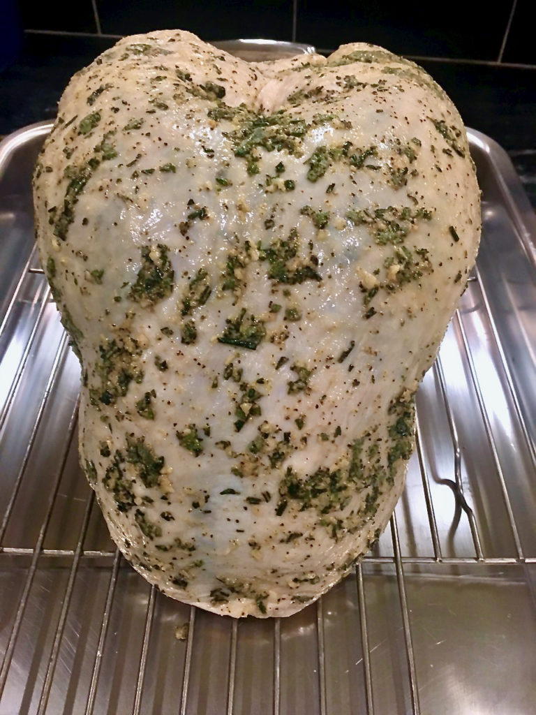 raw turkey breast in a baking pan covered with herbs