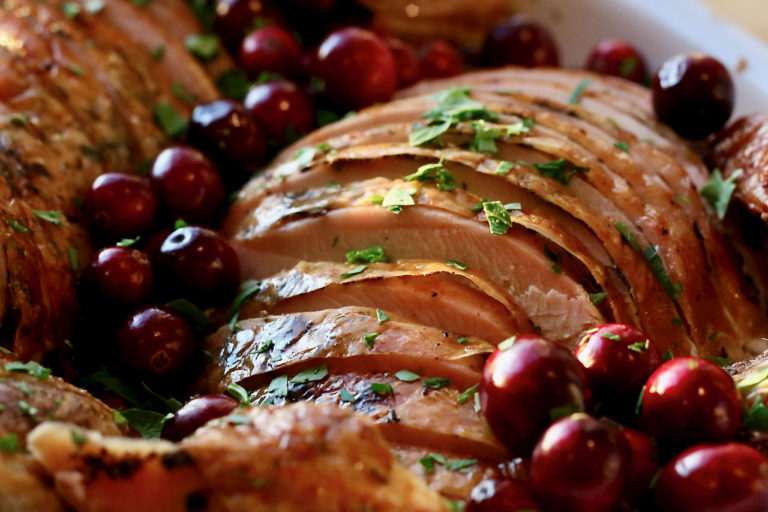 Sliced herb roasted turkey breast on a platter garnished with whole cranberries and parsley