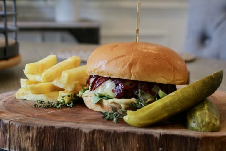 red wine onion burger with fries and a pickle on a wooden board