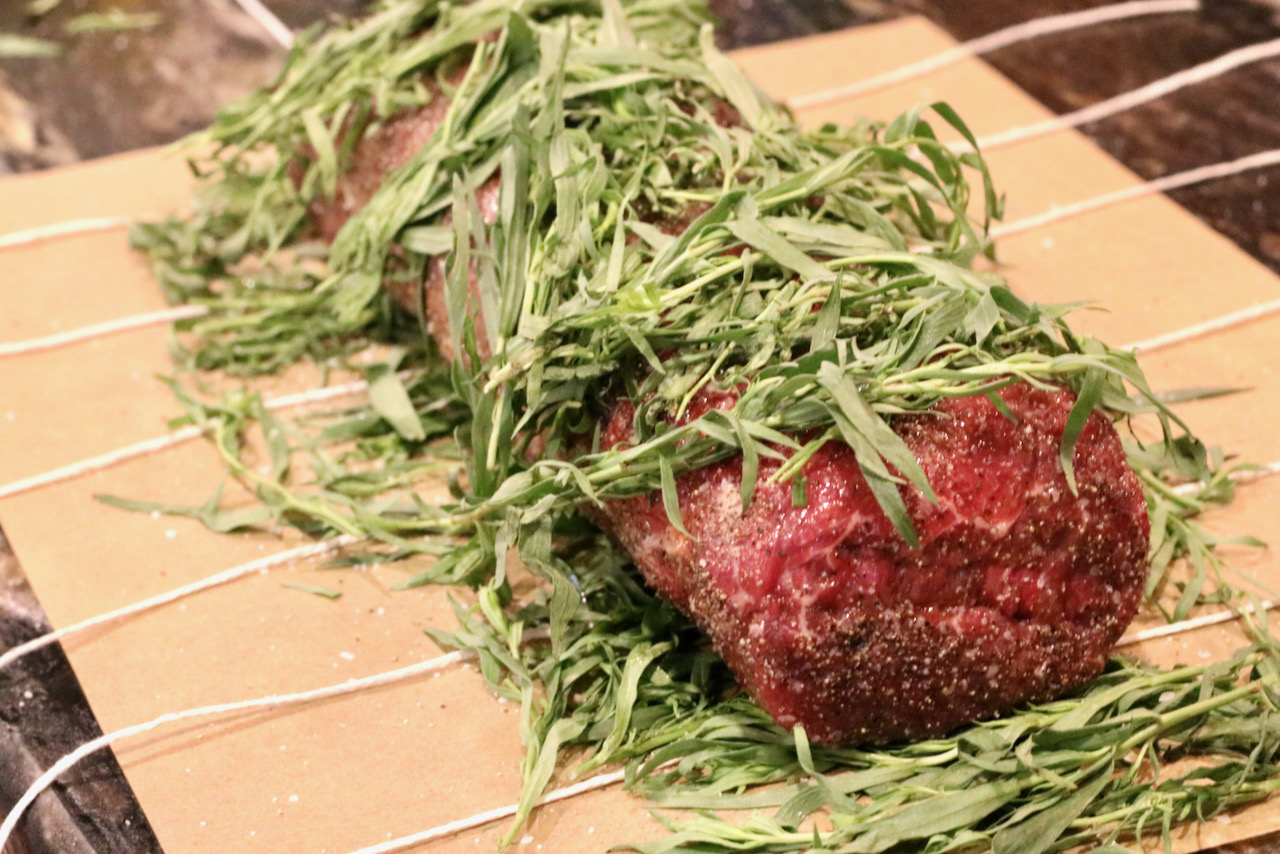 Raw piece of beef tenderloin being wrapped in tarragon