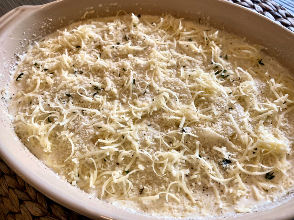 Sliced potatoes in gratin dish with cream and cheese