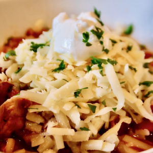 bowl of chicken chili topped with shredded cheese and sour cream