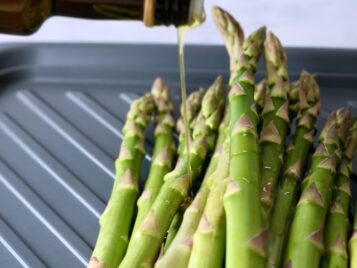 Asparagus on a plate and olive oil being drizzled over the asparagus