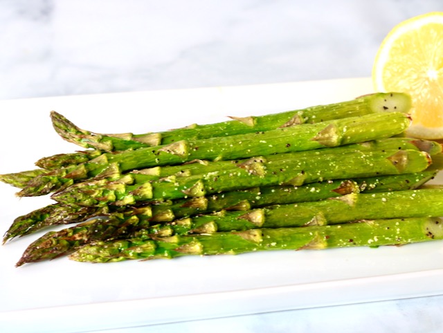Plate of roasted asparagus on a white place with a halved lemon on the plate