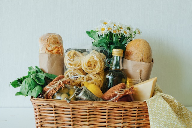 talian food basket with bread, basil, olive oil, lemons, and a bottle of wine.