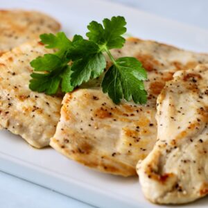 4 pieces of pan seared chicken on a white plate with a sprig of parsley