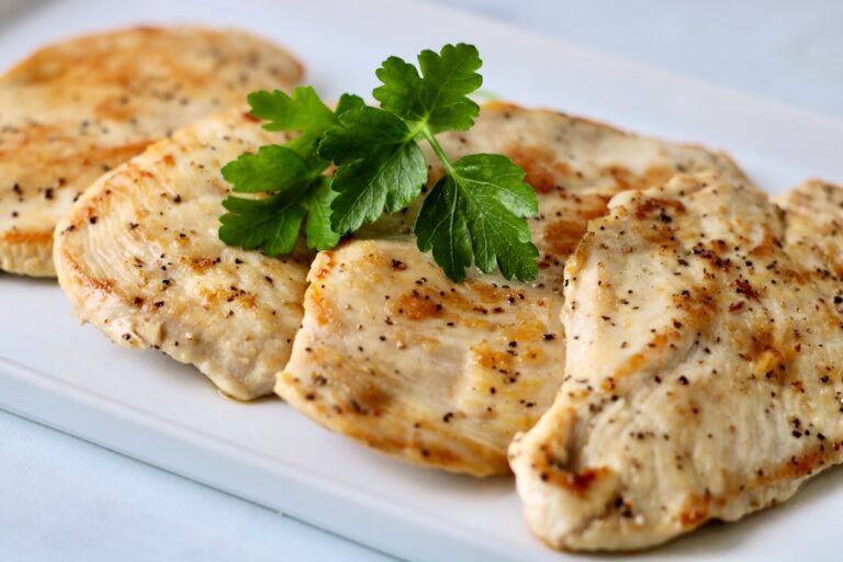 4 pieces of pan seared chicken on a white plate with a sprig of parsley