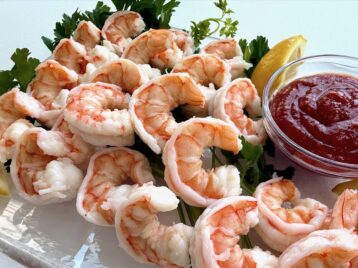 Shrimp cocktail on a clear platter with lemon wedges and cocktail sauce