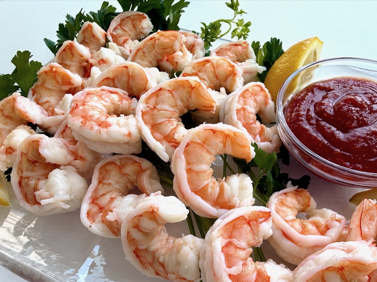 Shrimp cocktail on a clear platter with lemon wedges and cocktail sauce