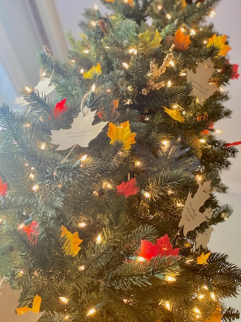 Christmas tree decorated for Thanksgiving with leaves, lights and custom cut outs with conversation starters and words of gratitude
