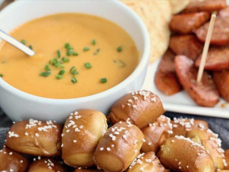 Homemade beer cheese dip served with warm pretzel bites and slices of sausage