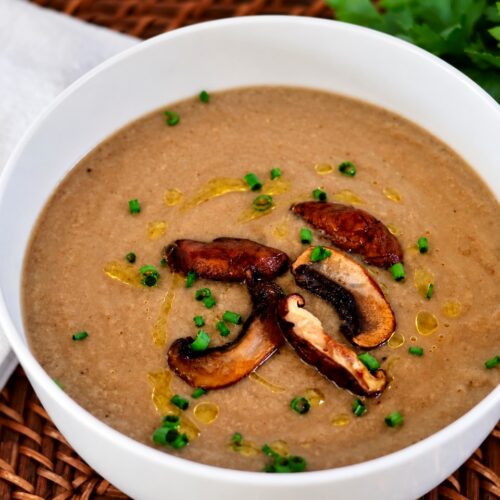 A bowl of portobello mushroom soup made without cream, topped with seared mushrooms, olive oil, and chives.