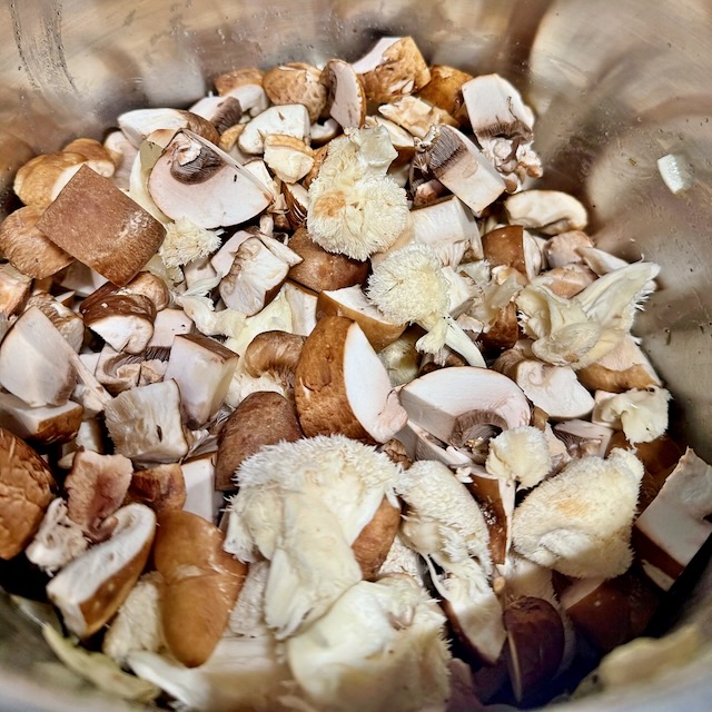 Chopped cremini, shiitake, and lion's mane mushrooms in a stainless steel stockpot for mushroom soup
