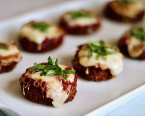 Mini Eggplant Parm garnished with basil on a serving tray- feature Image