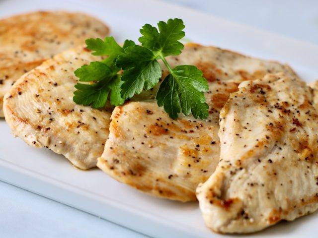 4 pieces of pan seared chicken on a white plate with a sprig of parsley