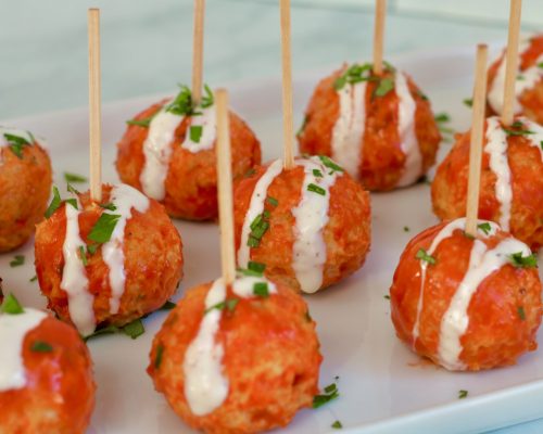 Slow cooker buffalo Chicken meatballs on a white platter with individual toothpicks and blue cheese dressing drizzled on top