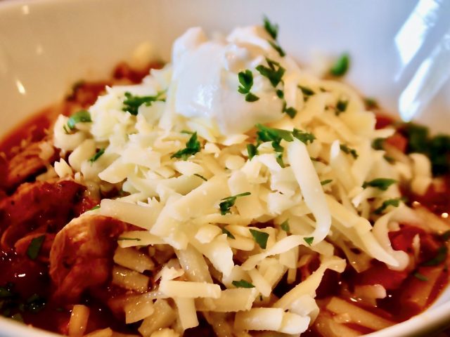 bowl of chicken chili topped with shredded cheese and sour cream