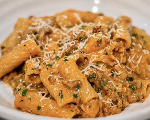 creamy sausage rigatoni recipe in a pasta dish sprinkled with parsley and parmesan cheese