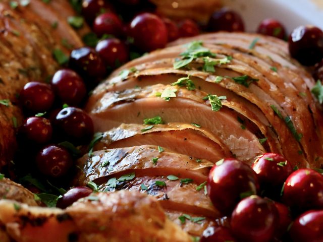 Sliced herb roasted turkey breast on a platter garnished with whole cranberries and parsley